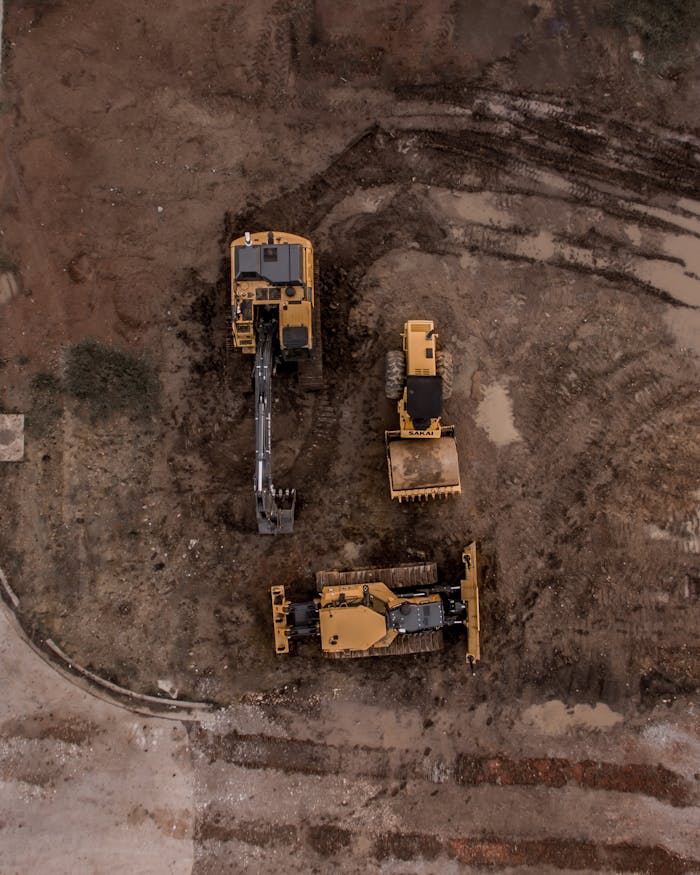 An aerial shot of heavy machinery at a construction site, including excavators and road rollers. Atlas Prime Building Contracting Dubai UAE